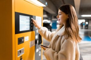 Elegant young girl pays for ticket in parking meter. Woman near terminal in the underground parking