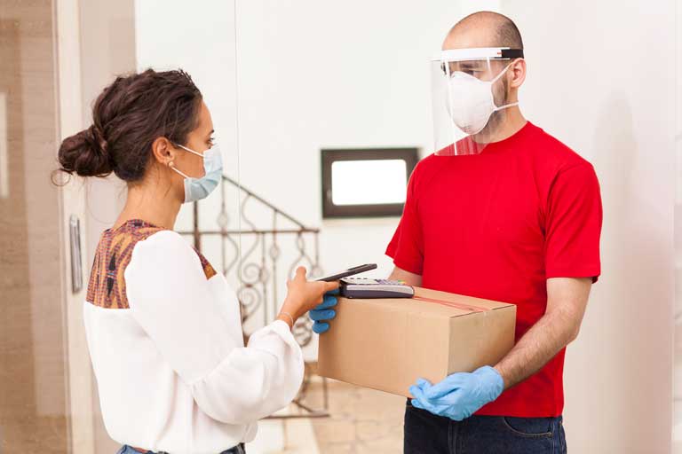Woman paying contactless for a delivery with a phone wearing a mask