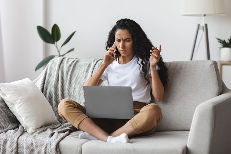 Frustrated woman talking on the phone with a laptop on her legs