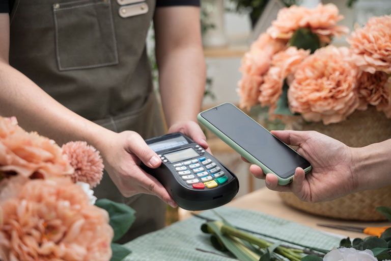 Woman at a flower shop paying for flowers by tapping her phone on contactless payment terminal
