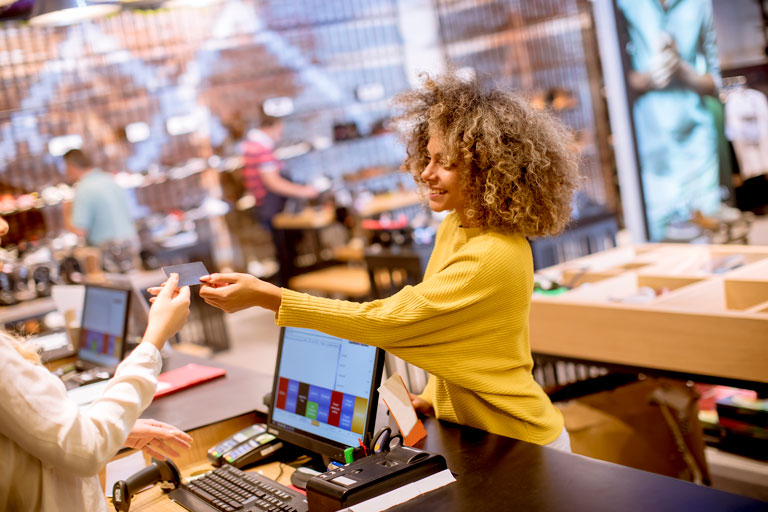 Young woman handing out a credit card to a cashier inside a clothing store