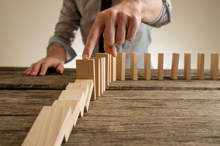 Man pushing small wooden blocks creating a domino effect