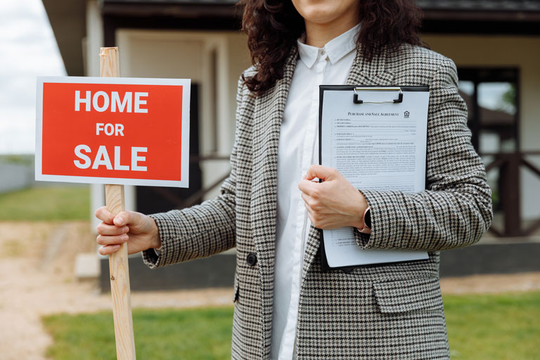 Realtor holding a home for sale sign in front of a house