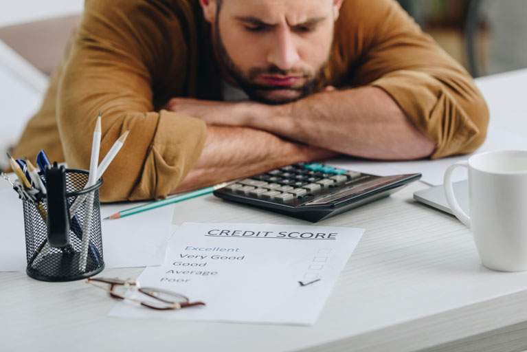 Frustrated man with his head on a table looking at a credit score printout with the word "poor" checked