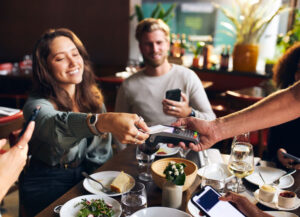 Woman paying with a credit card at a restaurant amongst friends
