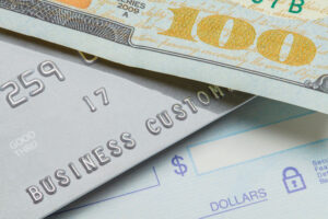Credit card in between a paper check and a 100 dollar bill