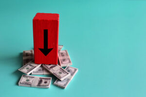 Red wooden cube with a black arrow pointing down on top of stacks of 100 dollar bills
