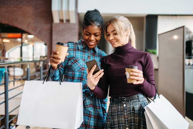 Two women taking a selfie with coffees and shopping bags in hand