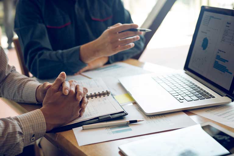 Two people taking notes and looking at graphs on a computer