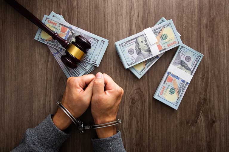 A man handcuffed with money and a gavel on the table
