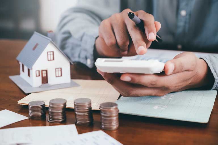 Man sitting down typing on a calculator with coins and a small house around