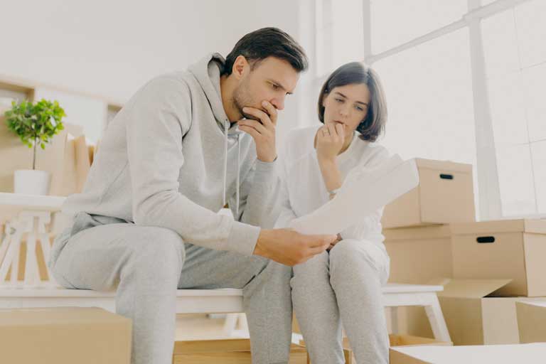 Worried couple reading a letter inside a house with moving boxes around them