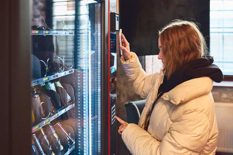 Young woman paying for a snack at a vending machine using contactless method of payment with mobile phone