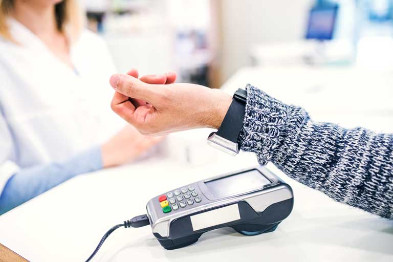 Woman making a payment by holding her smartwatch over a payment terminal inside a pharmacy