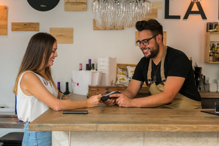 Cafe owner holding a payment terminal for a female customer paying with her credit card