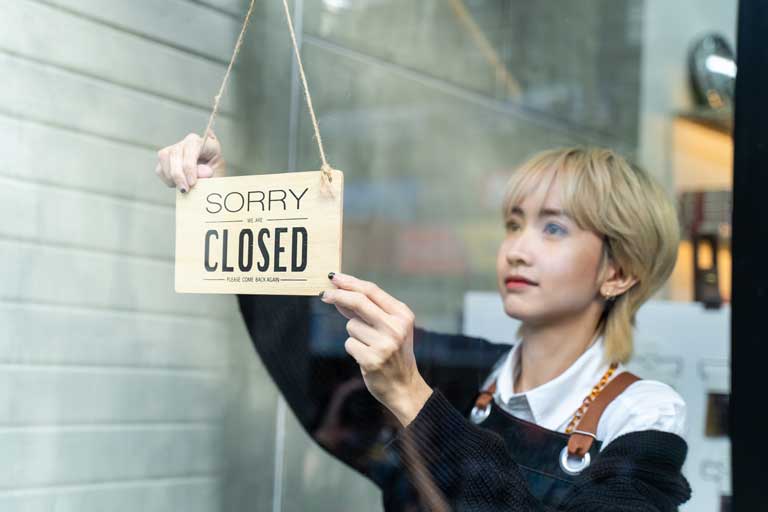 Young barista flipping a sorry we're closed sign