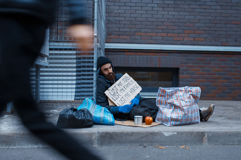 Homeless man sleeping on the floor holding up a sign with the words lost my job, my family ,my house