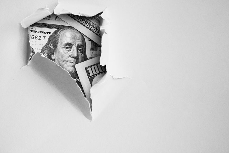 Hundred dollar bills behind a broken white wall