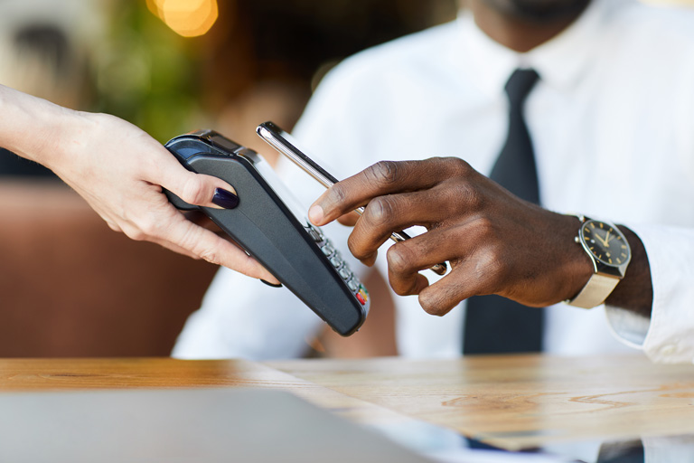 African american businessman paying at a cafe by holding his smartphone over a contactless payment terminal