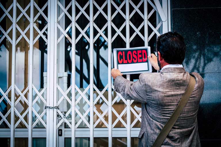 Male Business owner putting a closed sign on his business front door after closing down due to no business