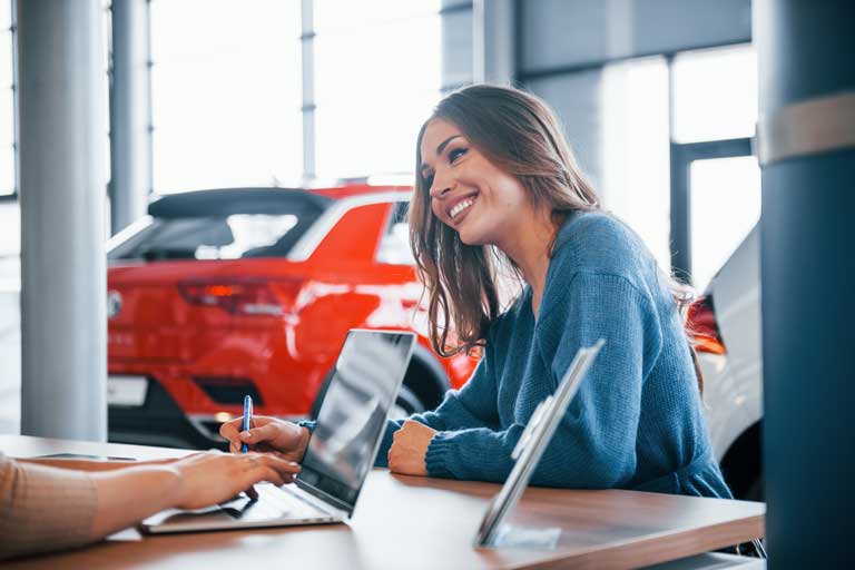 Woman sitting down signing paperwork at a car dealership