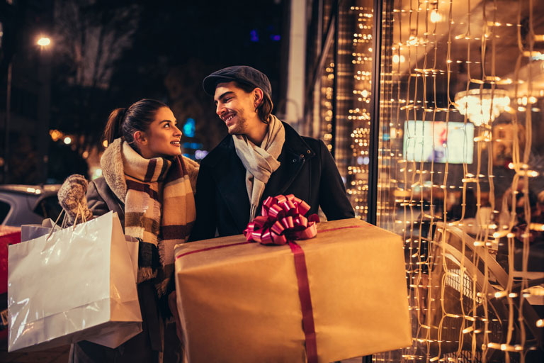Couple walking in front of a store while holding christmas presents