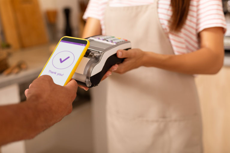 Woman holding a point of sale terminal for a customer paying with his smartphone