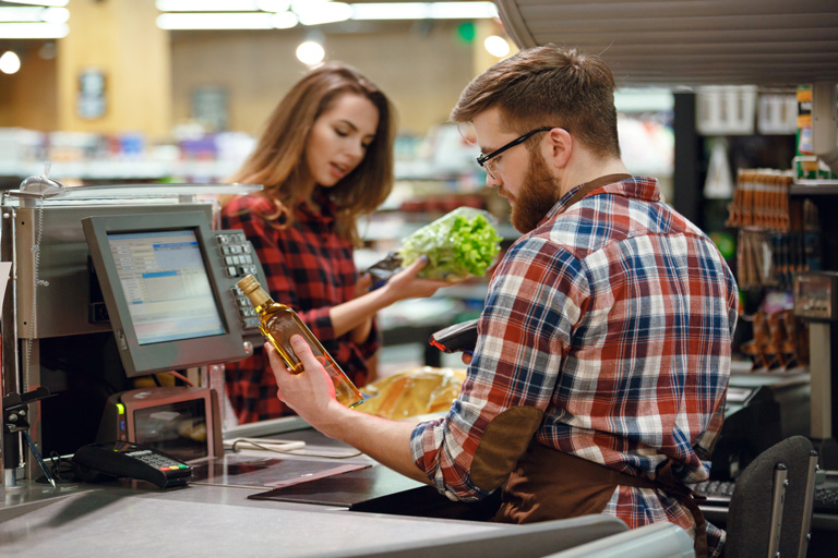 Cashier helping a customer check out while holding a bottle of vinegar