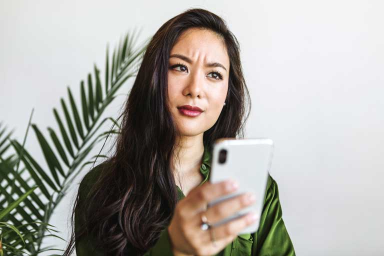 Worried young woman looking away from her phone while holding it