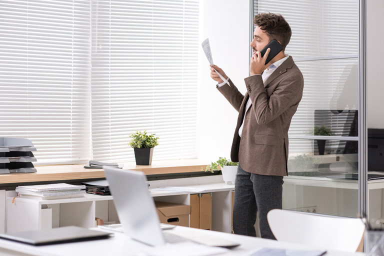Business professional talking on the phone inside an office while looking at a document