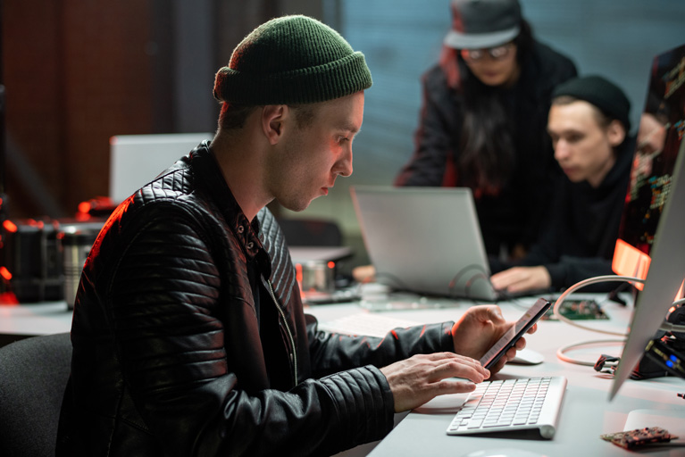 3 hackers inside a room checking their laptops and phones