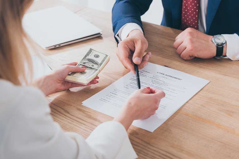 Loan officer handing out a pen to a woman for her to sign a loan agreement with cash in her hand