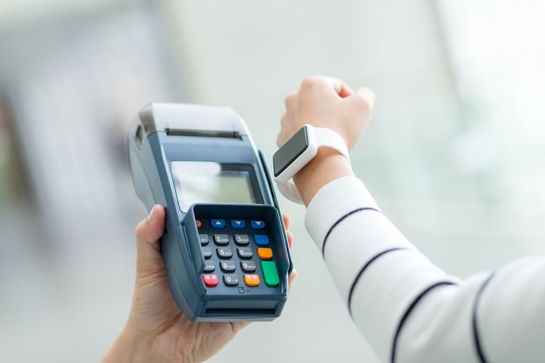 Woman holding her smartwatch next to a contactless payment terminal