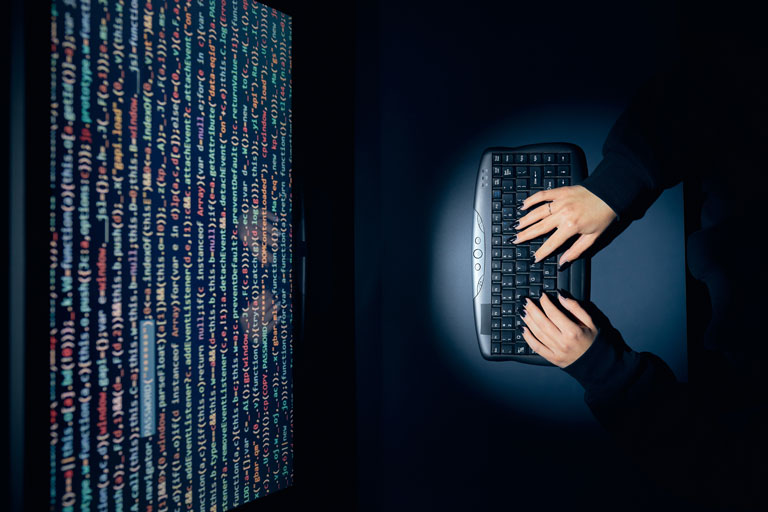 Woman sitting in a dark room coding in a computer