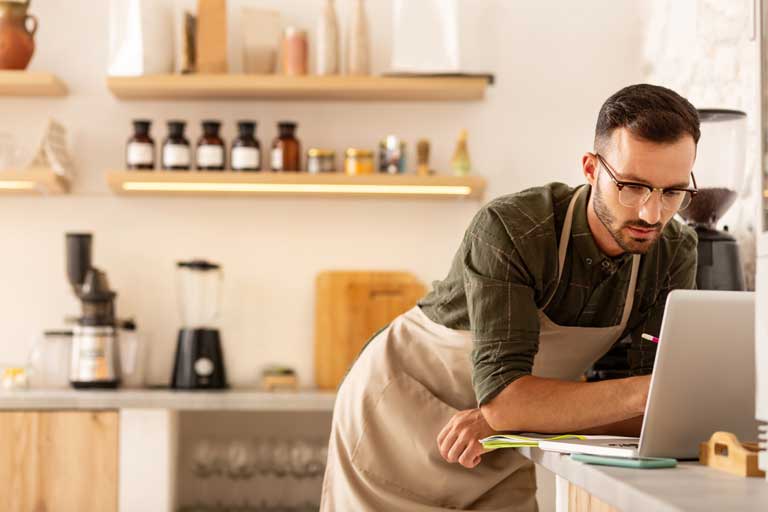 Male Cafe owner checking expenses on a laptop inside his business