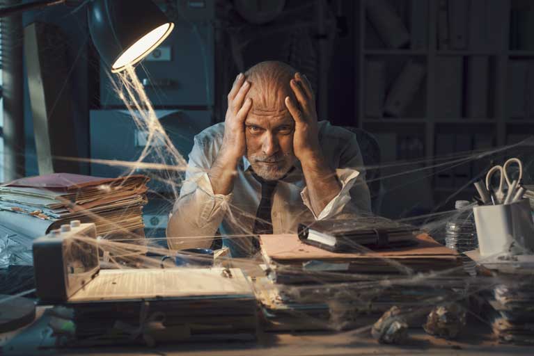 Desperate man in a dark room holding his head with spiderwebs on his desk
