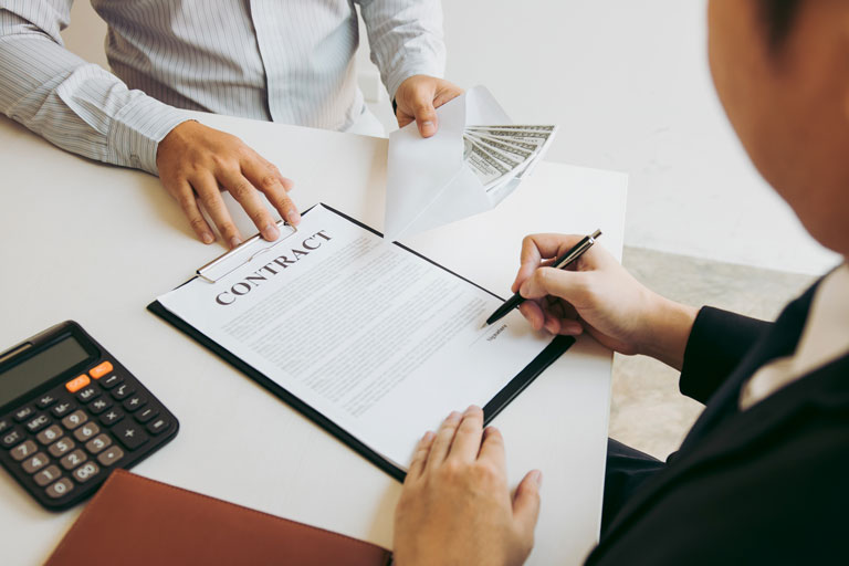 Man signing a financial contract while being handing out an envelope full of cash by the loan officer