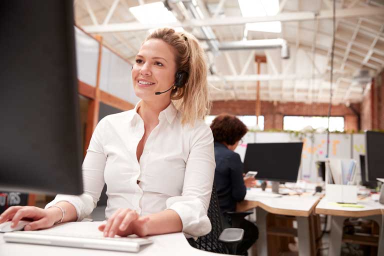 Female customer service representative speaking through a headset while typing on a computer