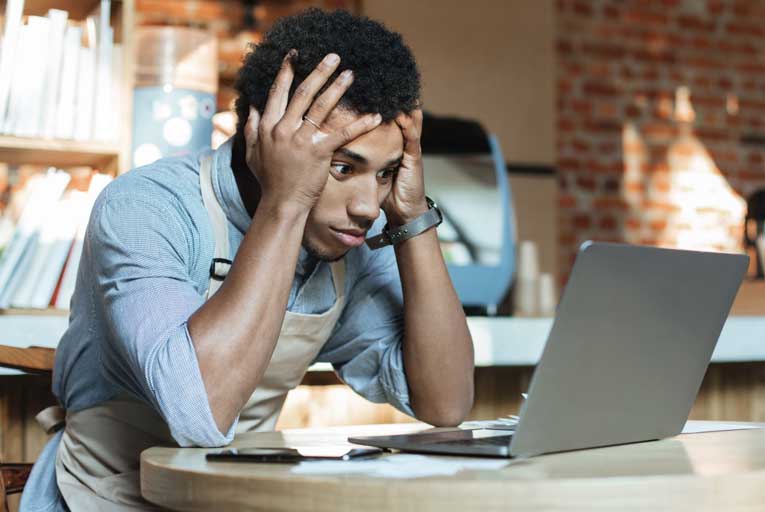 Frustrated business owner looking at a laptop with his hands on his head