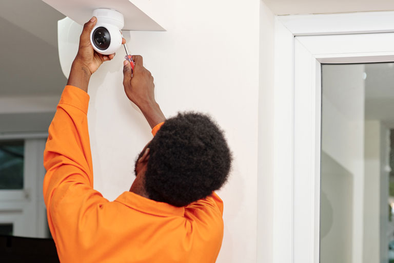 Male technician with an orange shirt fixing a camera inside a house