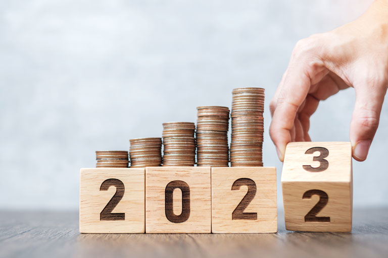 Hand holding wooden blocks with the number 2023 and coins on top