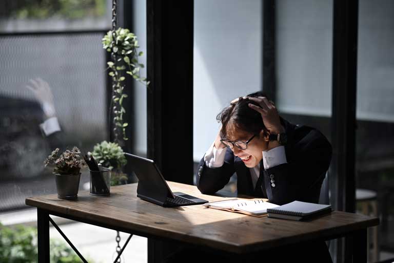 Frustrated businessman holding his head looking at a laptop inside his office