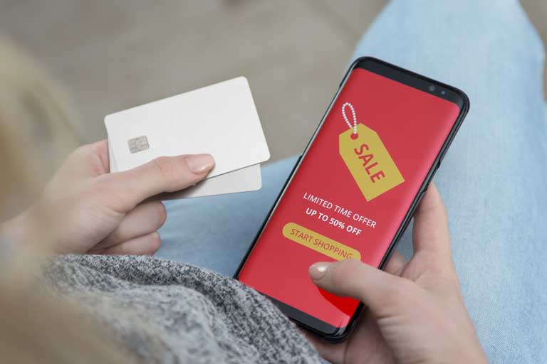 Woman making a purchase online with her phone while holding 2 white credit cards