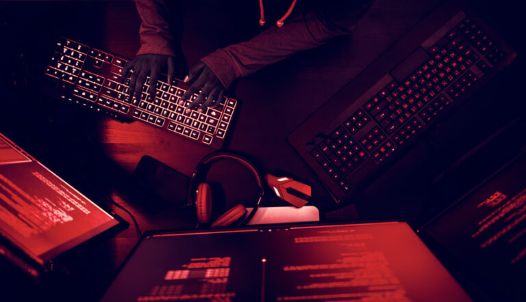Hacker with black gloves sitting inside a red room typing on a keyboard