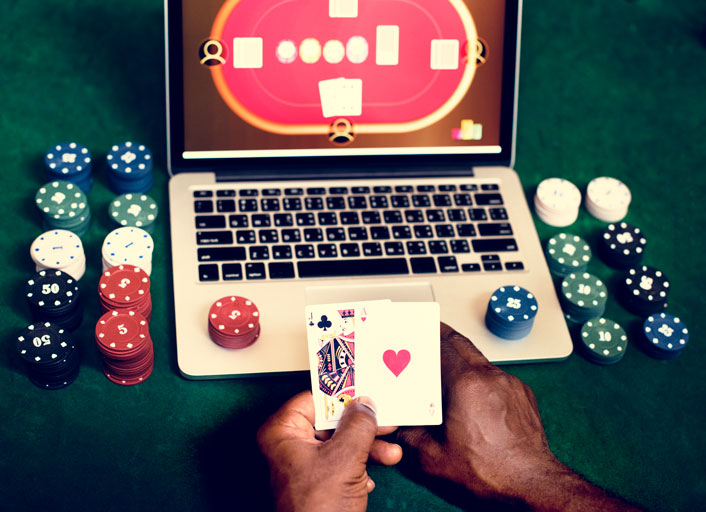 African american man playing poker online with chips around the computer