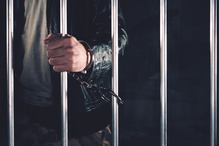 Adult male handcuffed to the bars of a prison cell