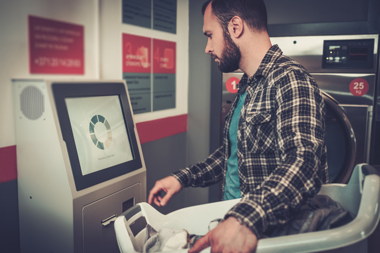 Man paying at a laundromat through payment kiosk with a touchscreen