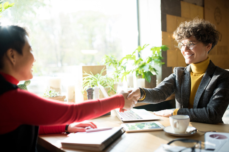 Two business woman shaking hands in a cafe