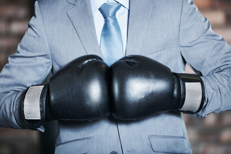 Business professional on a suit wearing black boxing gloves