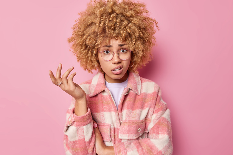 Surprised woman with curly hair raises hand